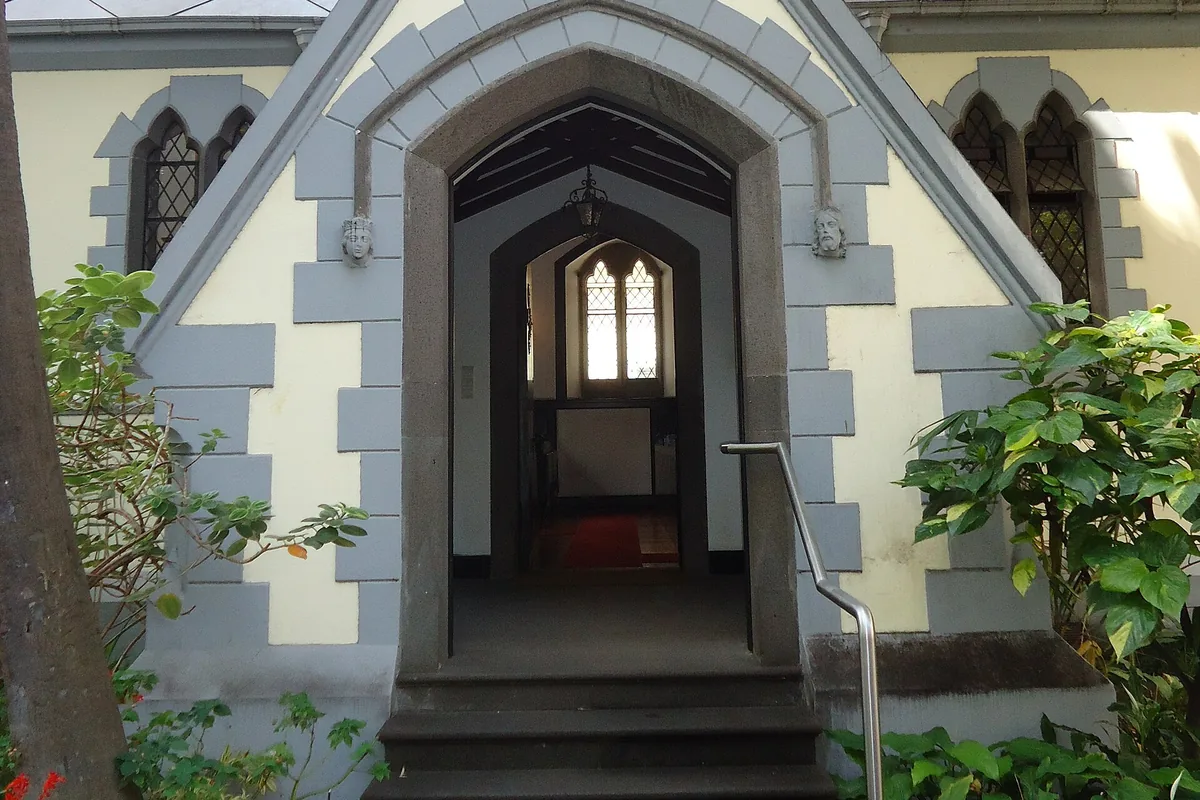 The pointed arched doorway of St Andrew's church framed by grey stone blocks, with steps leading up and shrubs on either side