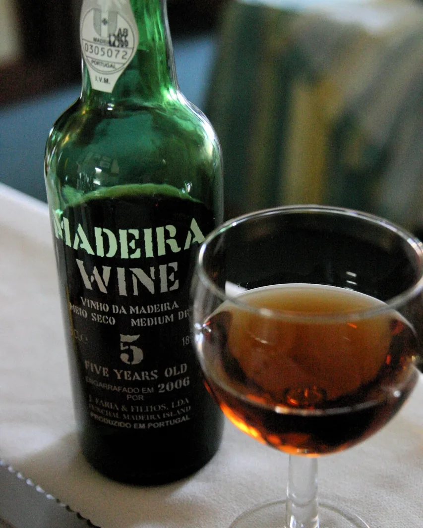A bottle and a glass of five-year-old Madeira wine standing on a table