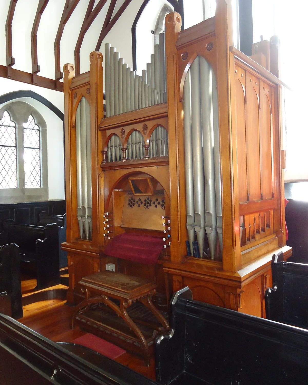 A carved wooden pipe organ with silver pipes in a neo-Gothic case standing beside a pointed window in the church